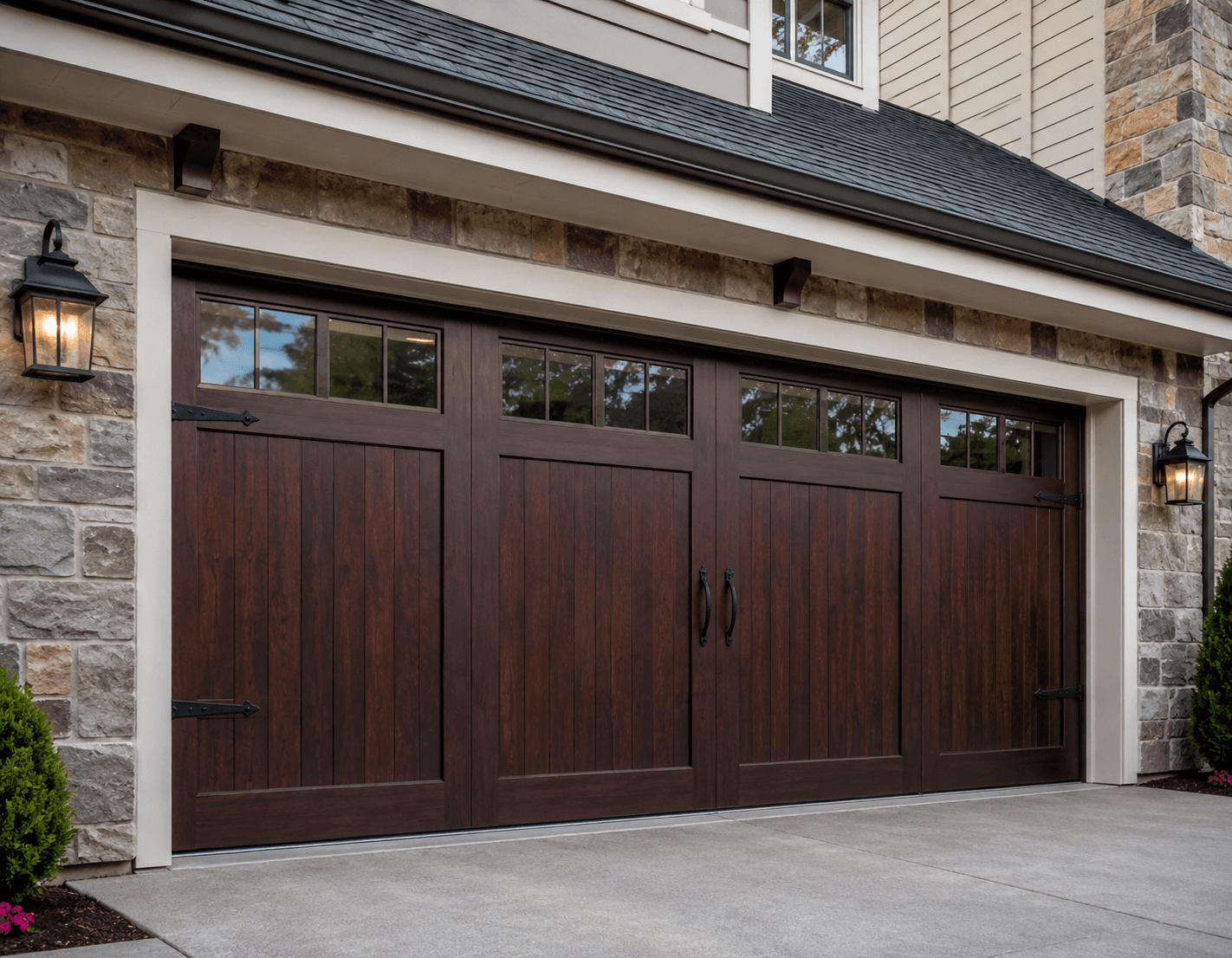 New dark wood carriage-style garage door with decorative hardware and upper windows on a stone-front home.